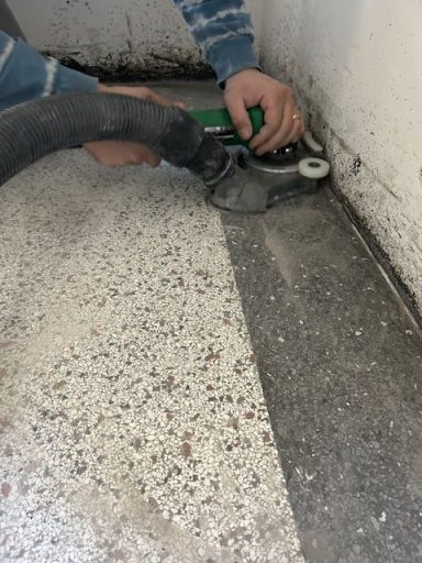 Een persoon maakt een vloer schoon met een stofzuiger in een hoek van de kamer.