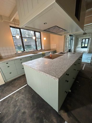 Moderne keuken met een groen keukeneiland en marmeren blad, nog in aanbouw.