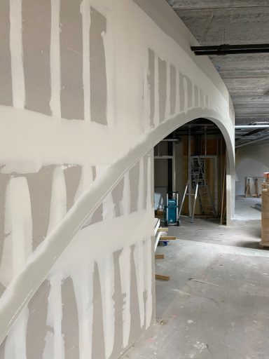 Gedeeltelijk afgewerkte muur met boog en bouwmaterialen op de achtergrond.
